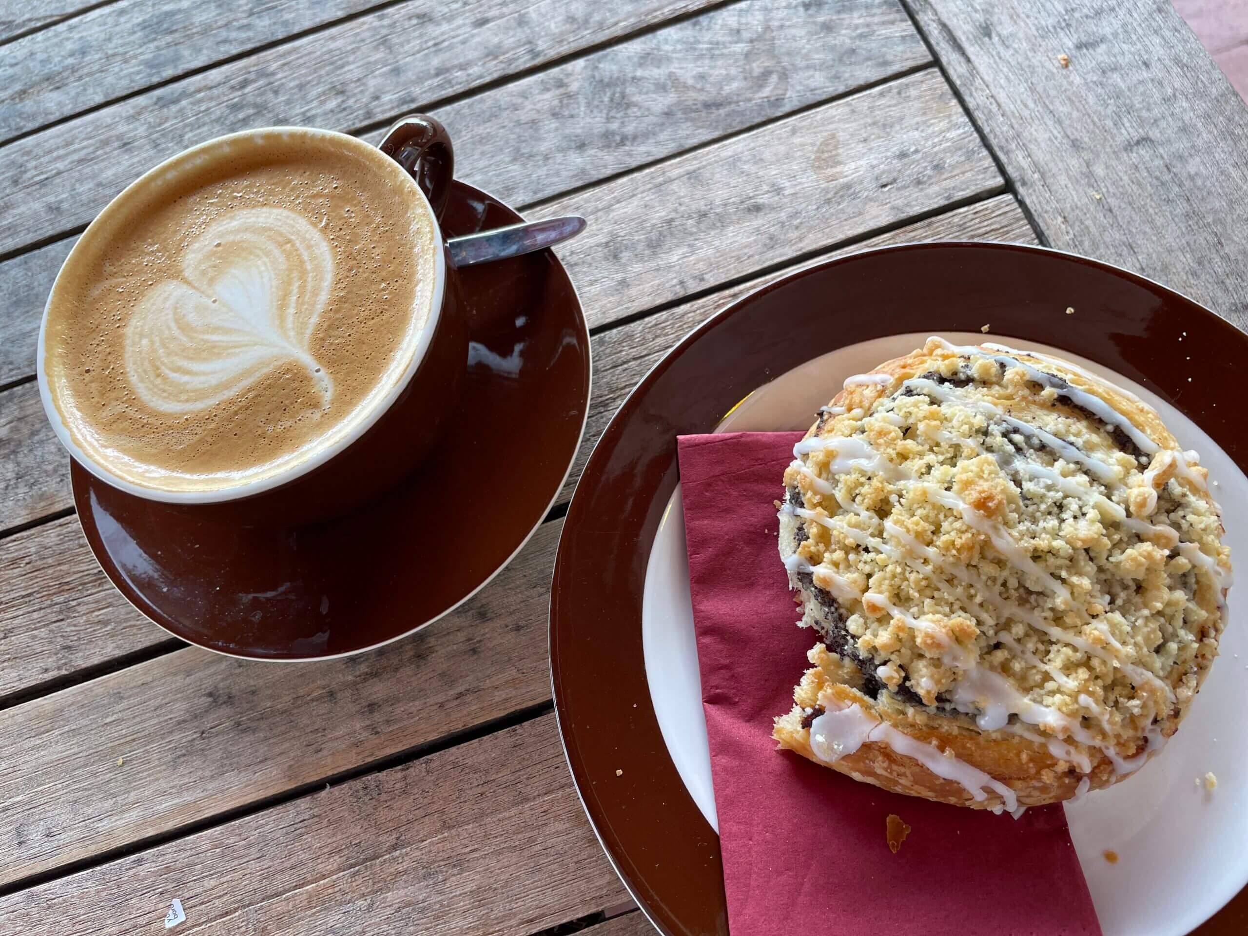 Cappuccino mit Latte-Art und hausgemachter Streuselkuchen auf braunem Teller – Genussmoment auf Spiekeroog.
