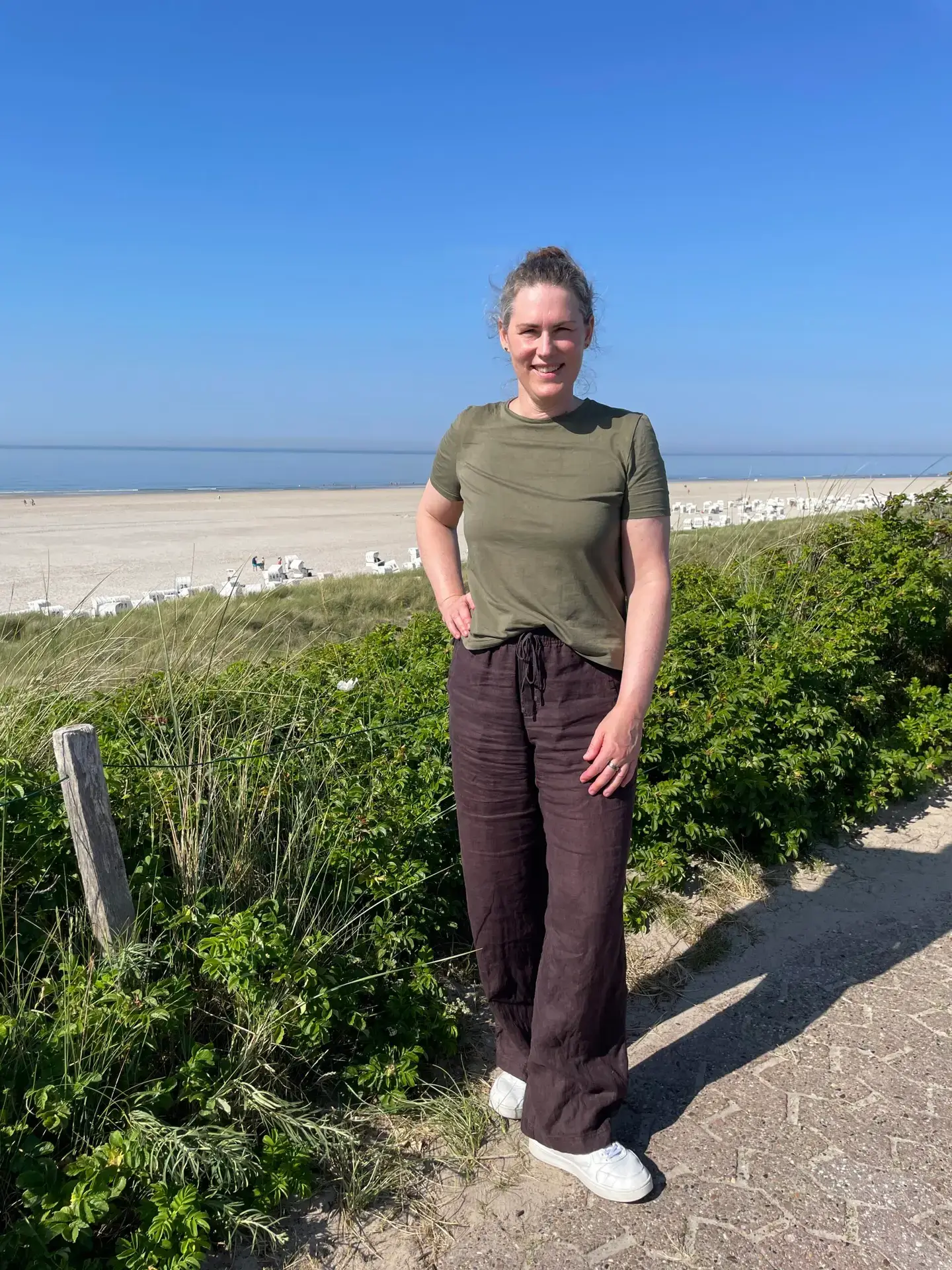 Frau steht lächelnd am Nordseestrand auf Spiekeroog, im Hintergrund Meer und Himmel