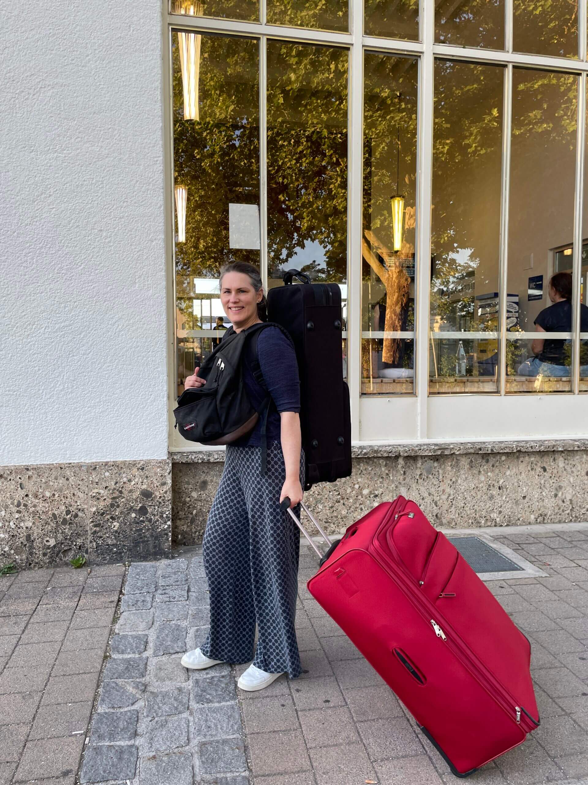 Frau mit großem roten Koffer, Rucksack und Saxophonkoffer am Bahnhof beim Aufbruch nach Spiekeroog