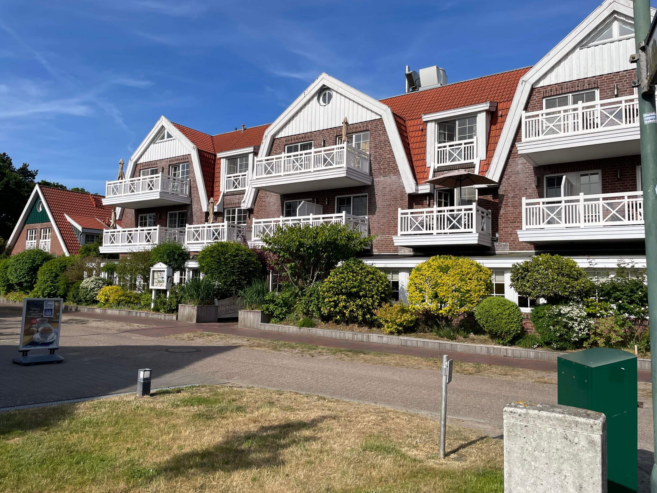 Hotel Spiekerooger Leidenschaft: Traditionelle Inselarchitektur mit roten Dächern, weißen Balkonen und üppigem Grün.