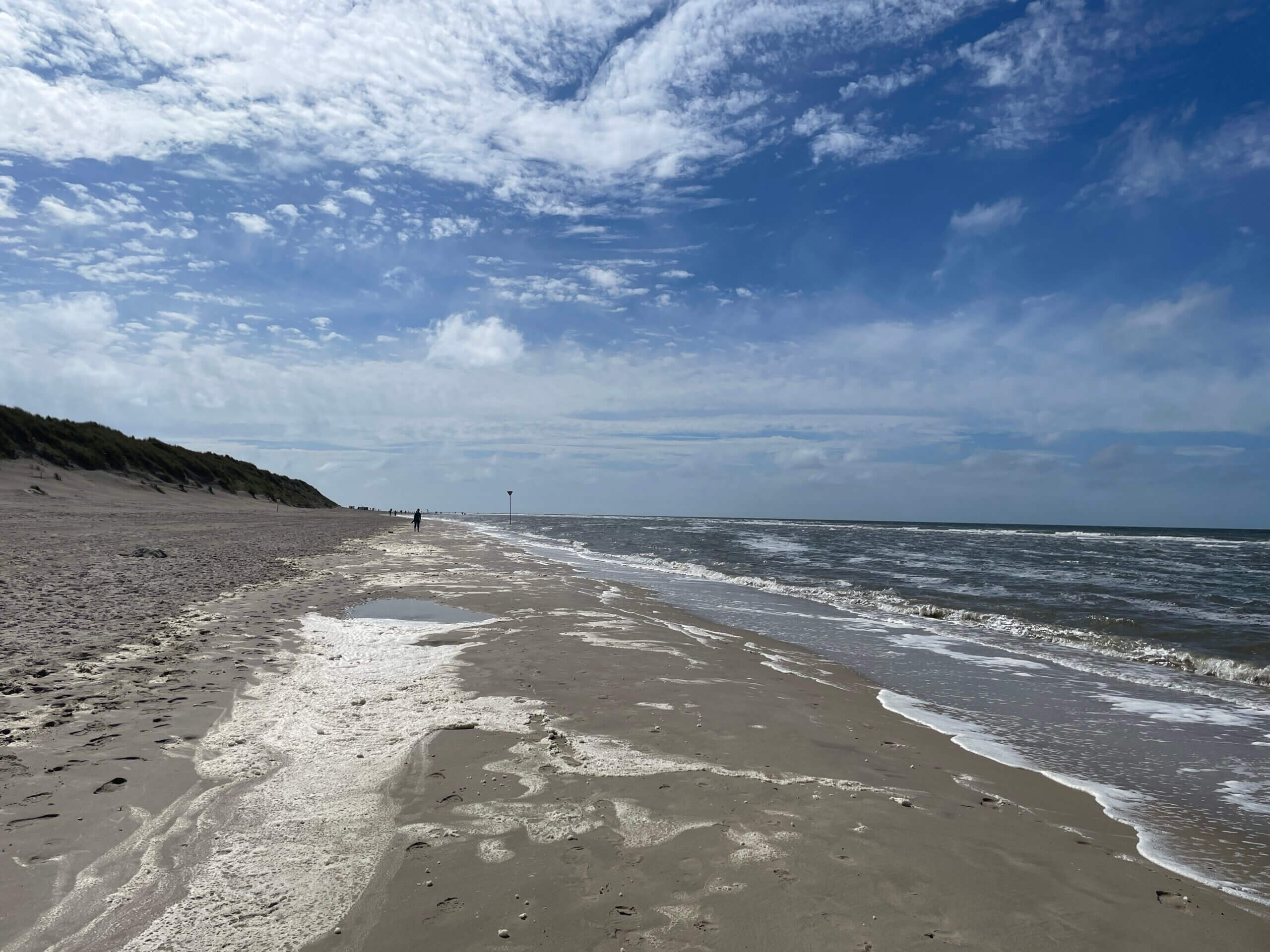 Endloser Nordseestrand von Spiekeroog mit Wellen und dramatischem Wolkenhimmel