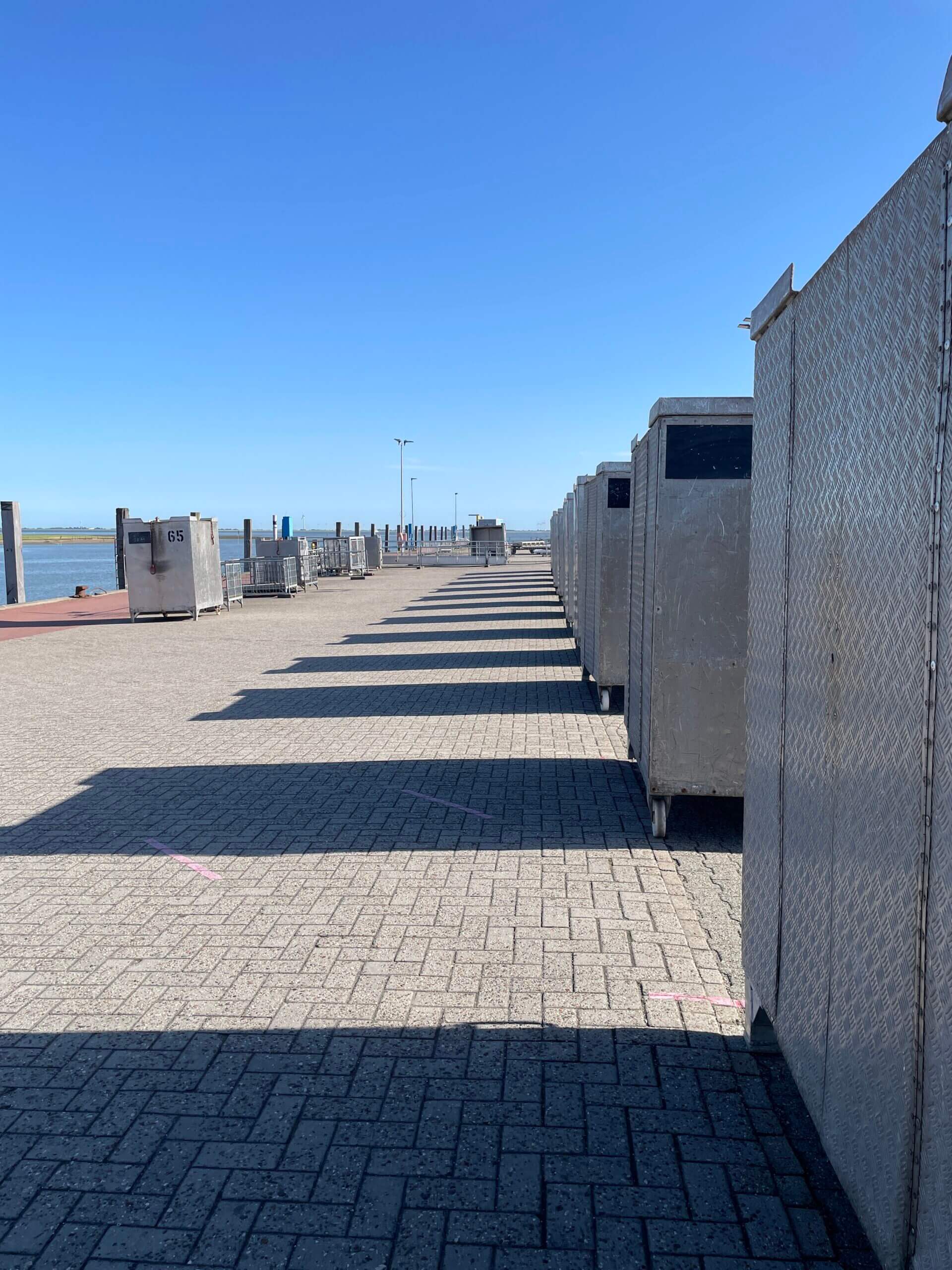 Reihe von Gepäckcontainern entlang eines gepflasterten Weges im Hafen Spiekeroog