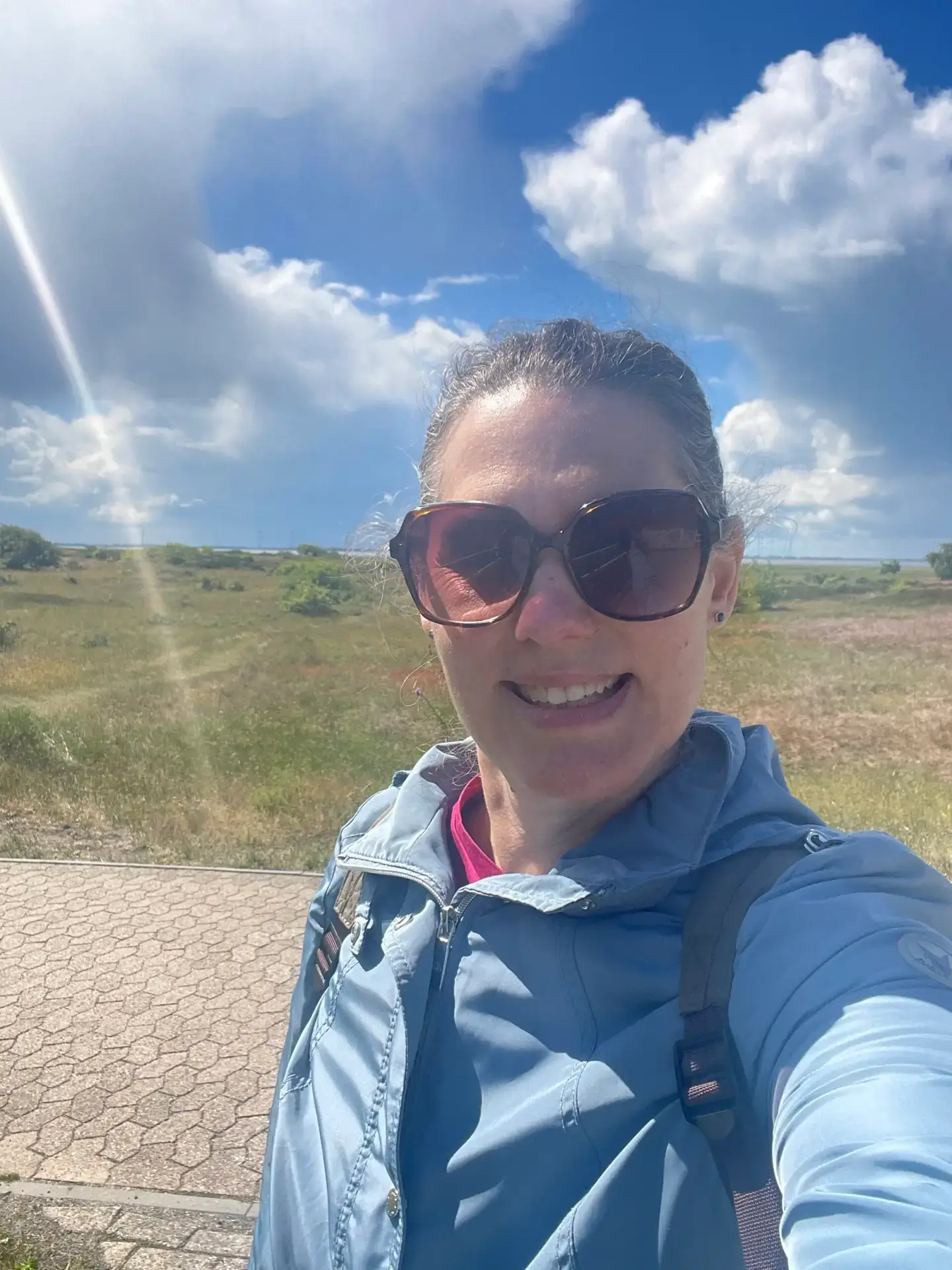 Lächelnde Frau mit Sonnenbrille vor Dünenlandschaft und blauem Himmel