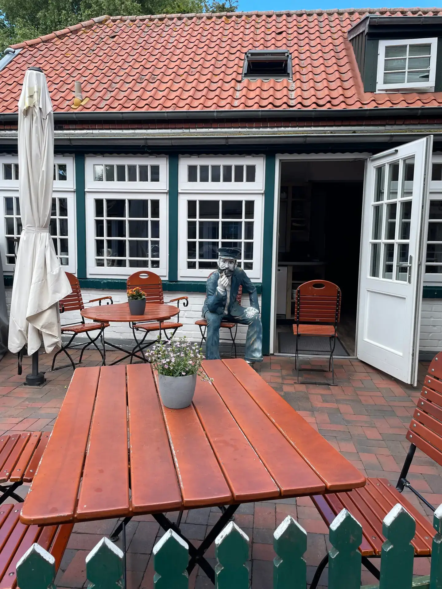 Friesisches Reetdachhaus mit blau-weißer Fensterfront und gedeckter Terrasse mit Sonnenschirm