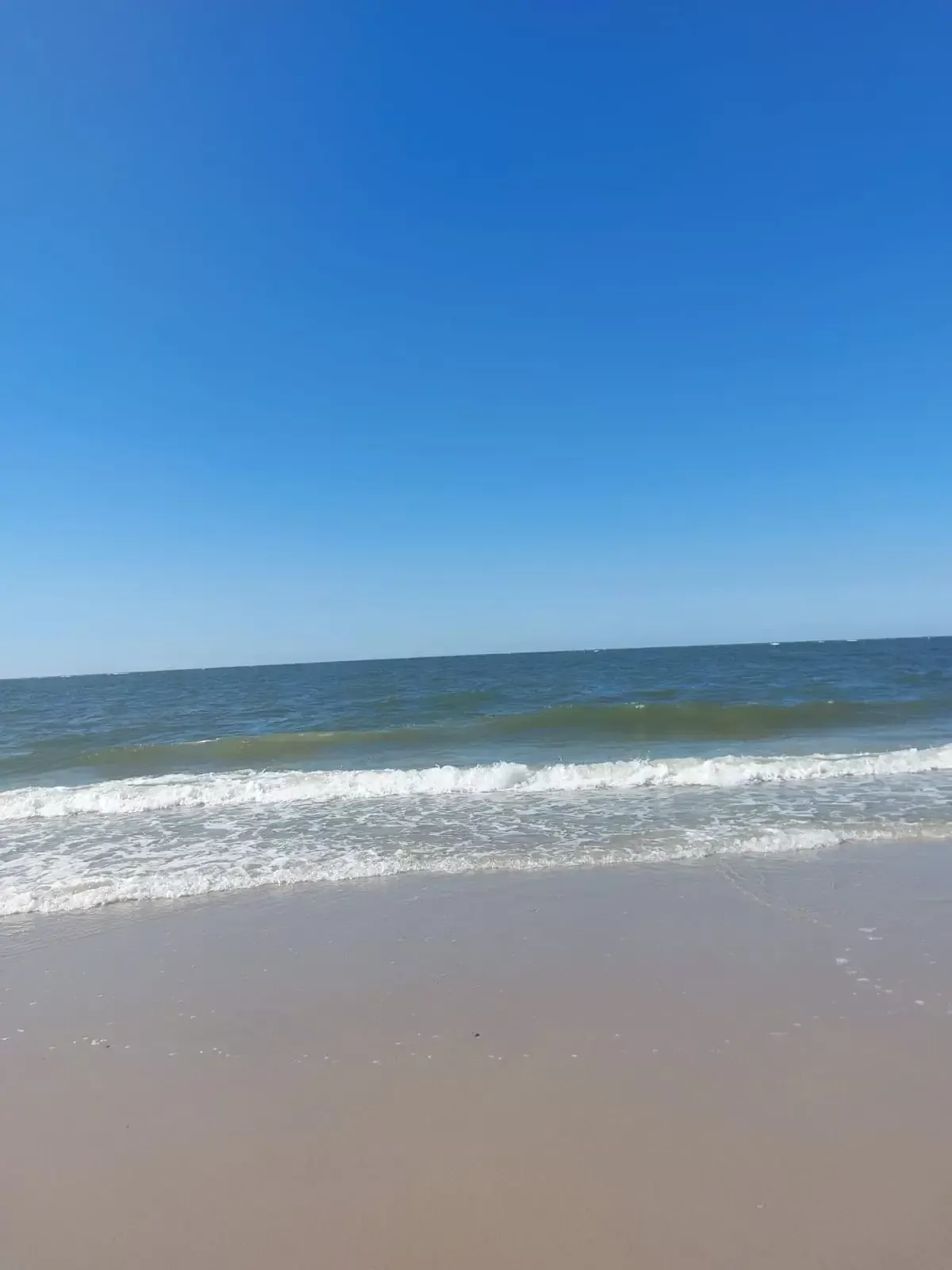 Nordseestrand mit sanften Wellen unter klarem blauem Himmel