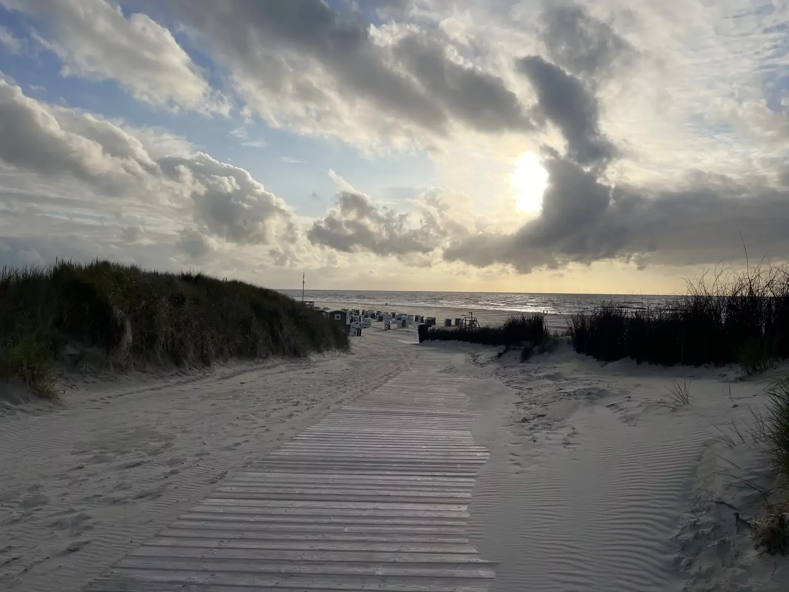 Bohlenweg durch die Dünen zum Strand, Sonne hinter Wolken